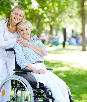Pretty nurse and senior patient in a wheelchair looking at camera outside