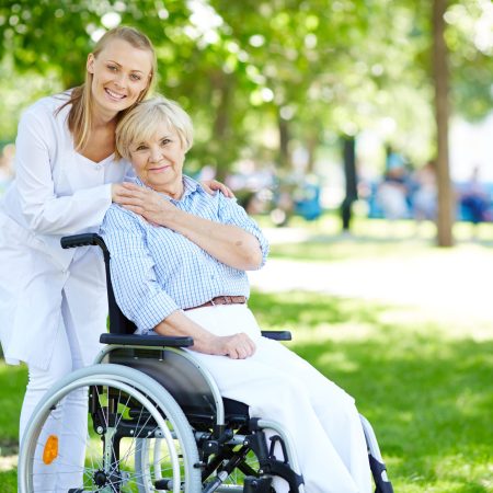 Pretty nurse and senior patient in a wheelchair looking at camera outside